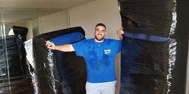 A man holding two mattresses in his arms.